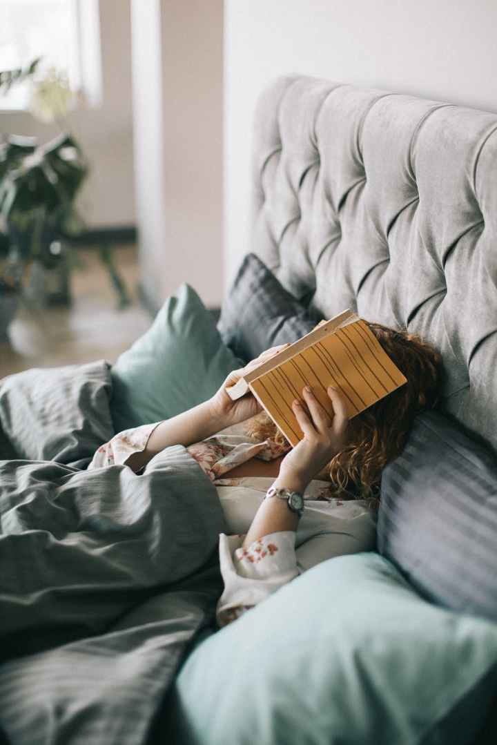 woman covering face with book on bed